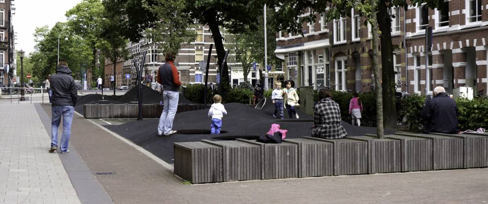 View of children playing and adults sitting on wooden bench seating