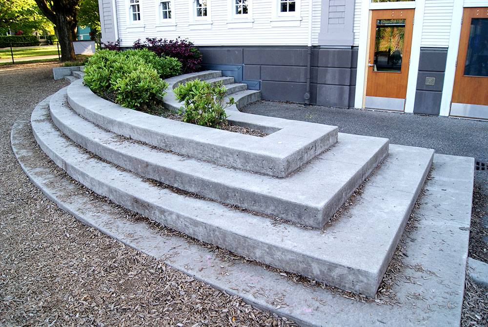 Stepped seating around a planter beside play equipment