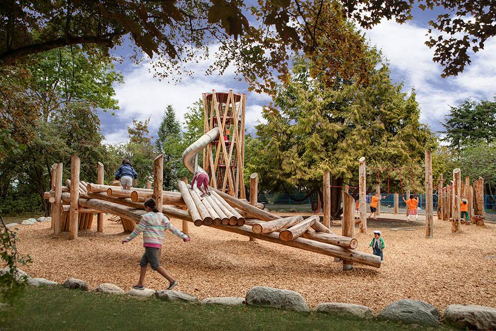 Children play on wood climbing structure over mulch