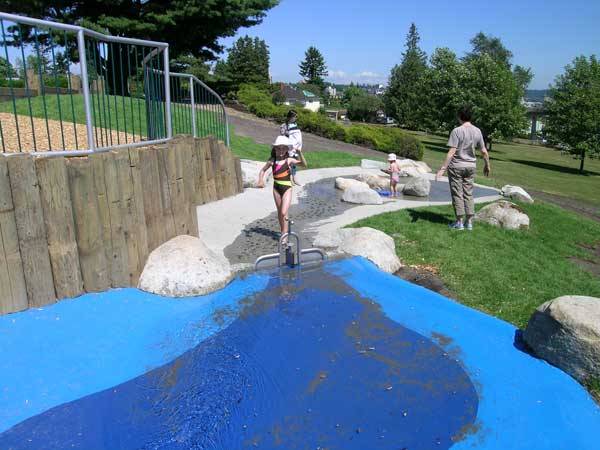 A metal railing separates the water play zone from an upper terrace