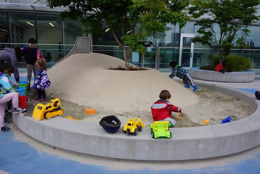 This sand play area features a poured rubber mound and shade tree in the middle