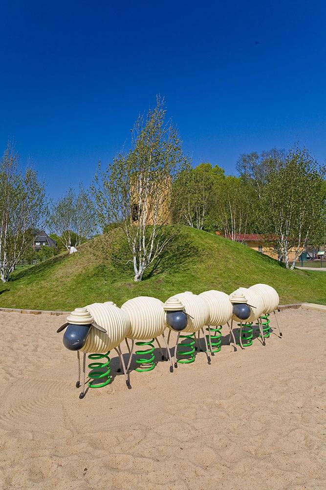 A row of sheep spring riders in front of a grass mound